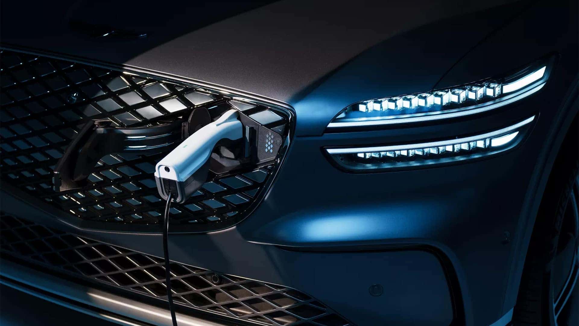 Close-up of the 2026 Genesis Electrified GV70 grille, illuminated Two-Line headlights, and integrated charging port