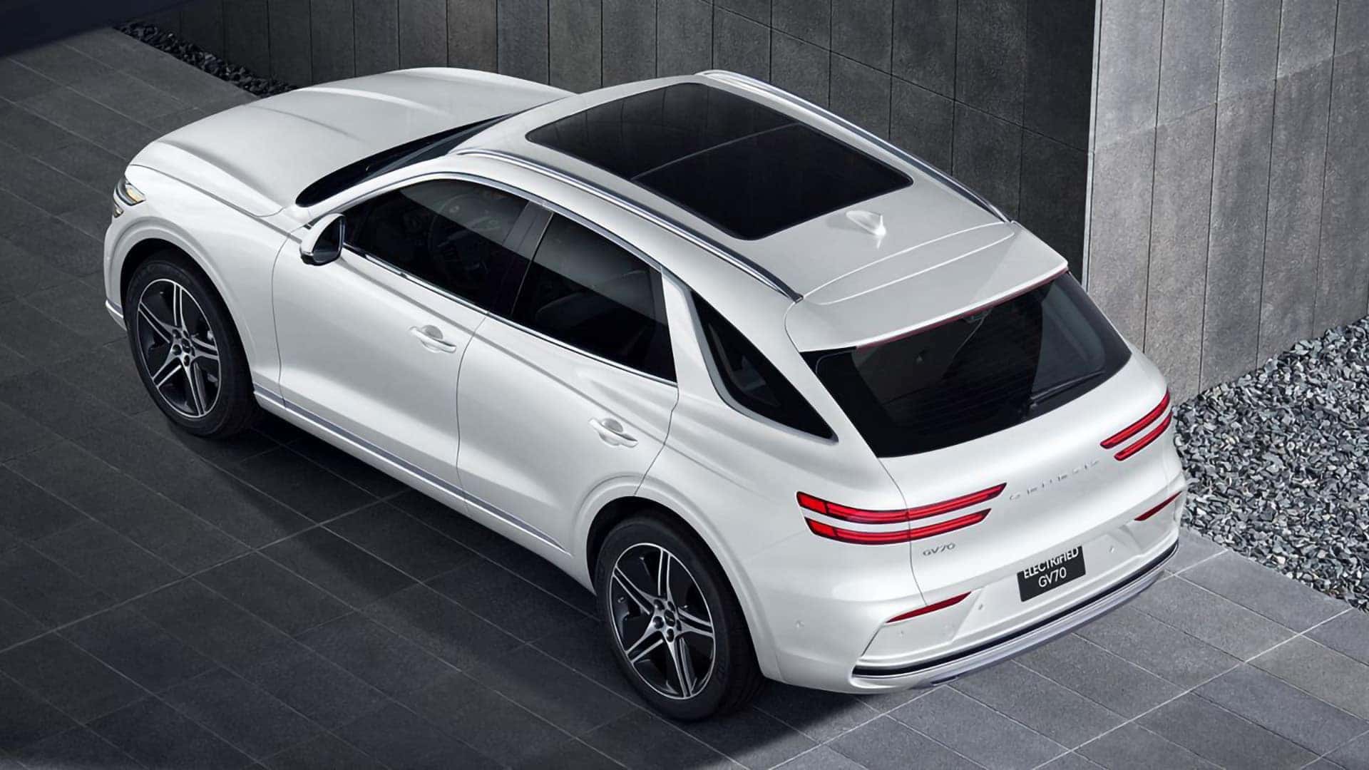 Overhead rear three-quarter view of a white 2026 Genesis Electrified GV70 with panoramic sunroof and roof rails