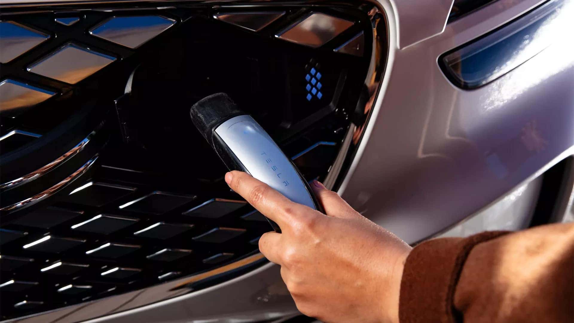 Driver connecting a charging cable to the front grille charging port of the 2026 Genesis Electrified GV70