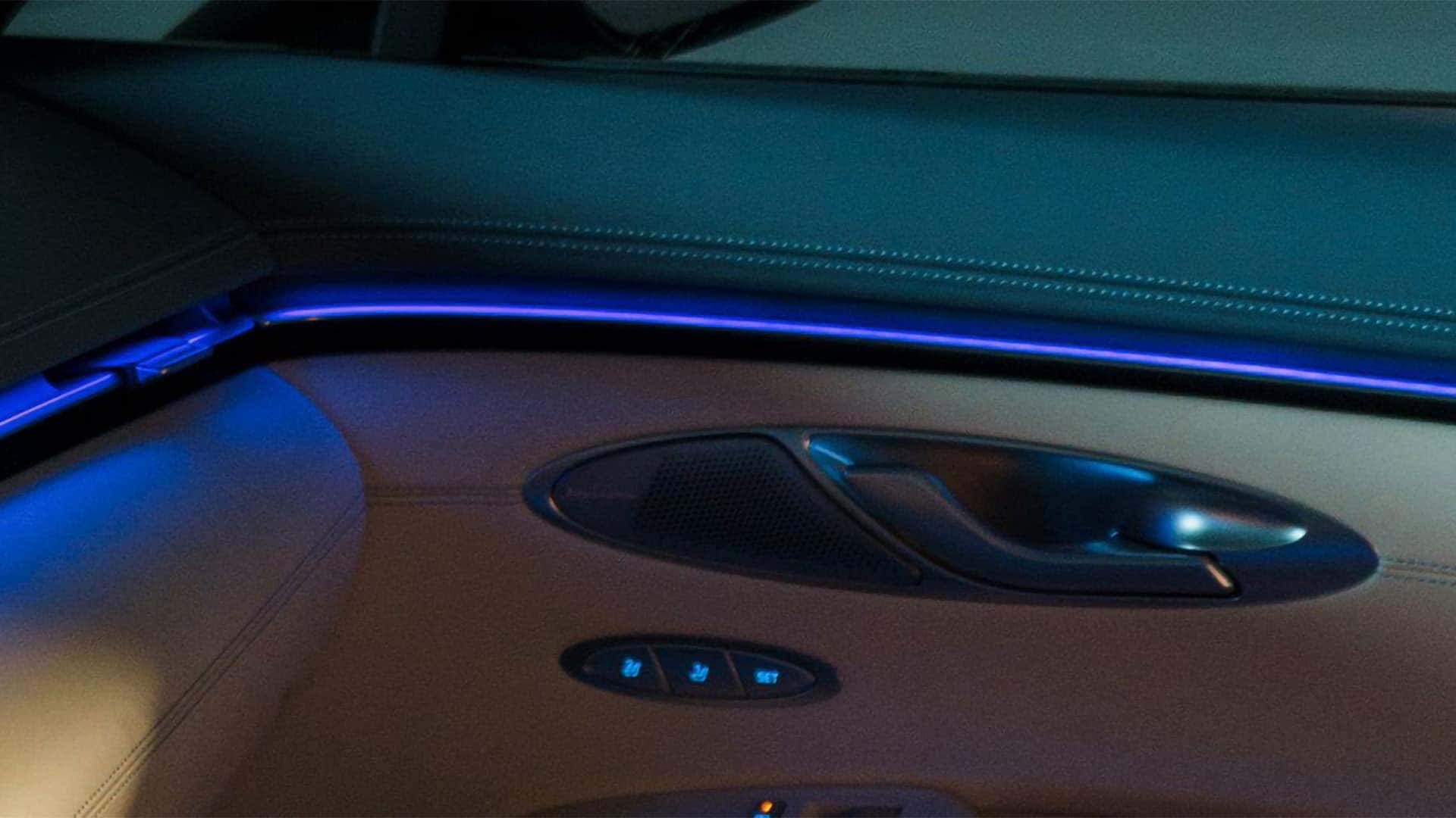 Blue ambient lighting along the 2026 Genesis Electrified GV70 door panel beside the speaker and seat memory controls
