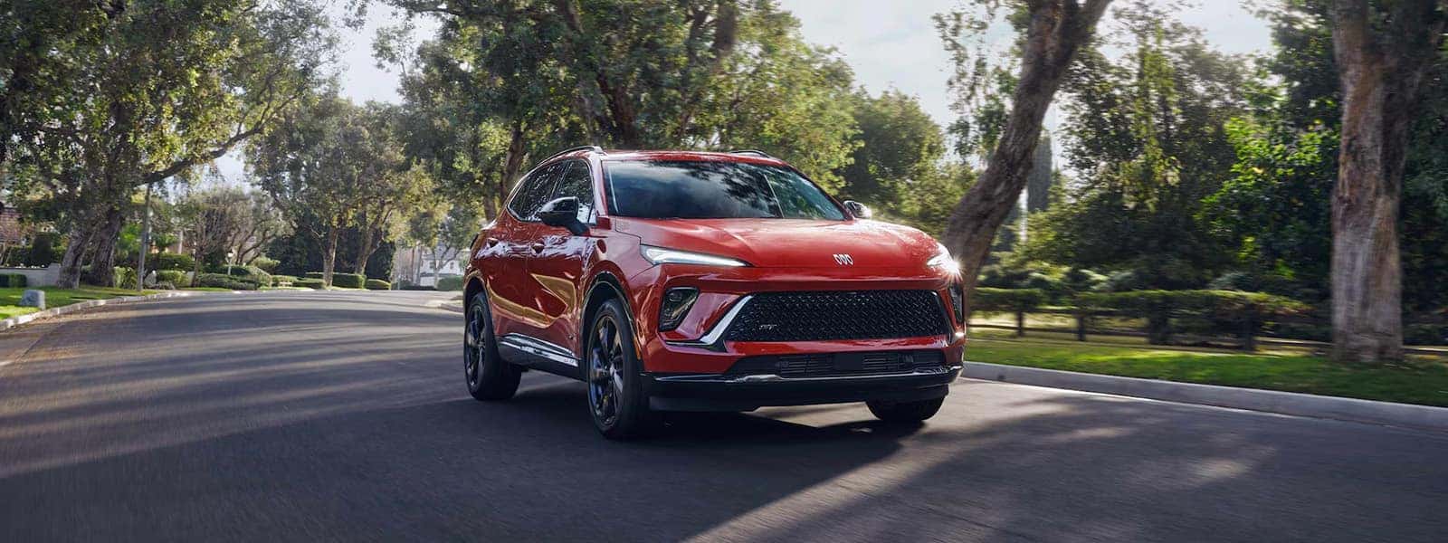 Red 2026 Buick Envision driving along a tree-lined residential road