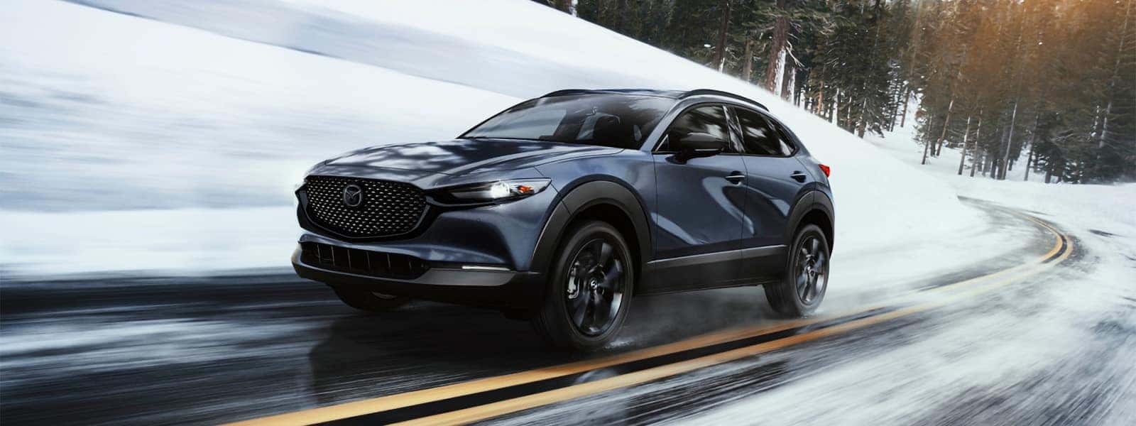 Dark blue 2026 Mazda CX-30 driving on a snow-covered mountain road