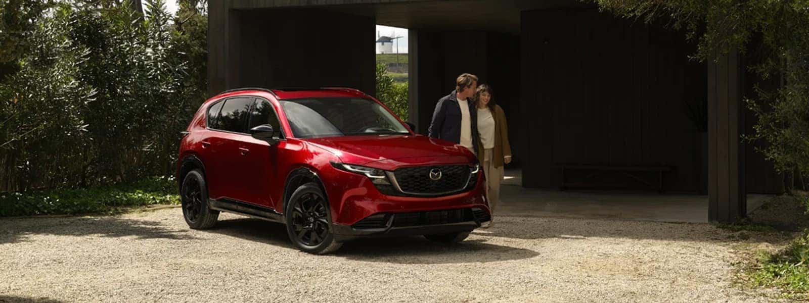 Red 2026 Mazda CX-5 parked outside a modern home with two people standing nearby