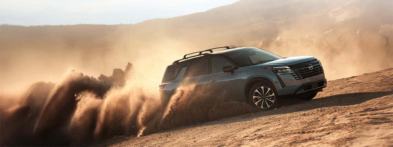 2026 Nissan Pathfinder driving across sandy terrain with dust trailing behind the three-row SUV