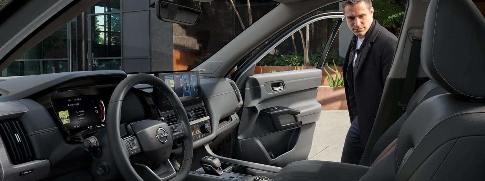 2026 Nissan Pathfinder front interior with digital displays, touchscreen, center console, and open passenger door