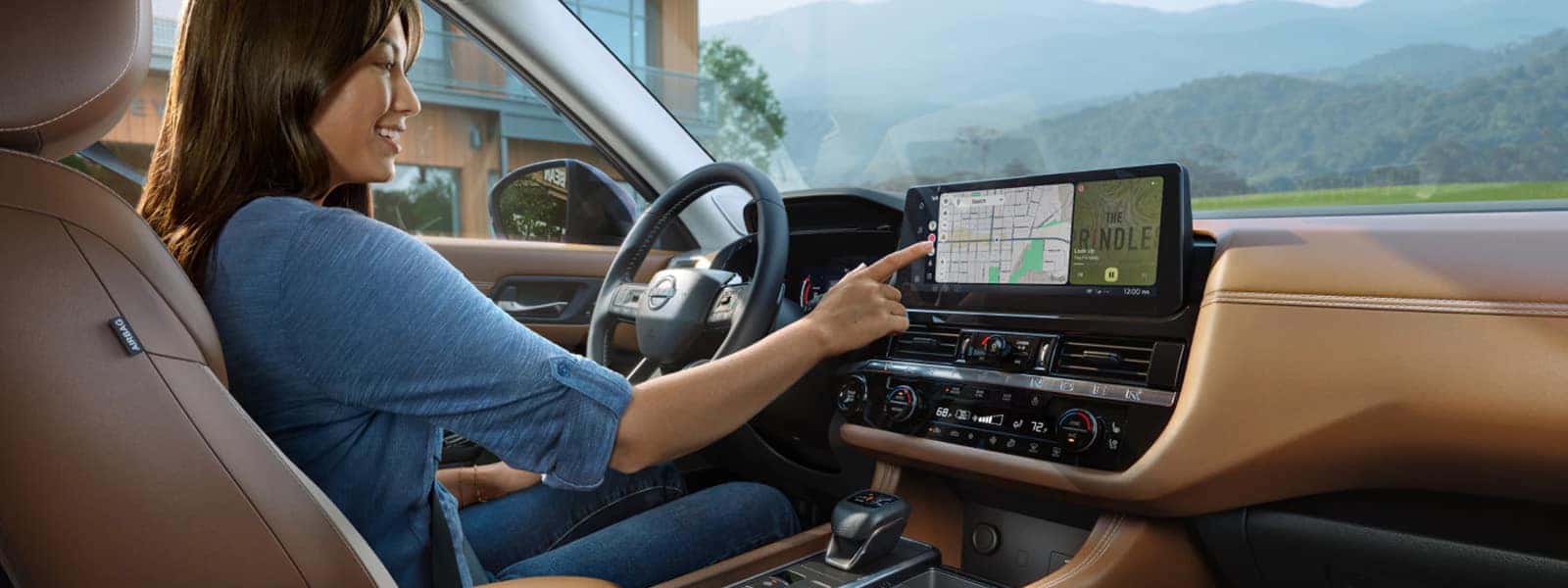 Driver using the 2026 Nissan Pathfinder touchscreen navigation system inside the SUV’s cabin