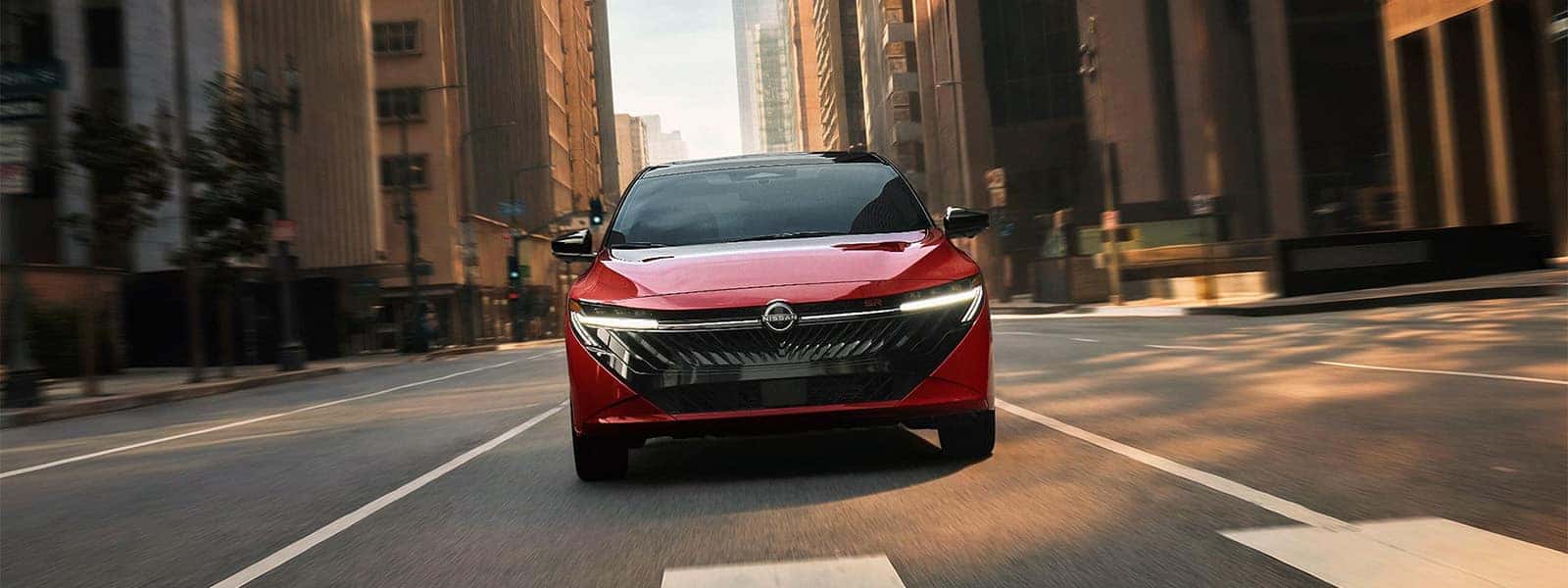 Red 2026 Nissan Sentra driving through a city, shown from the front with its grille and LED headlights visible.