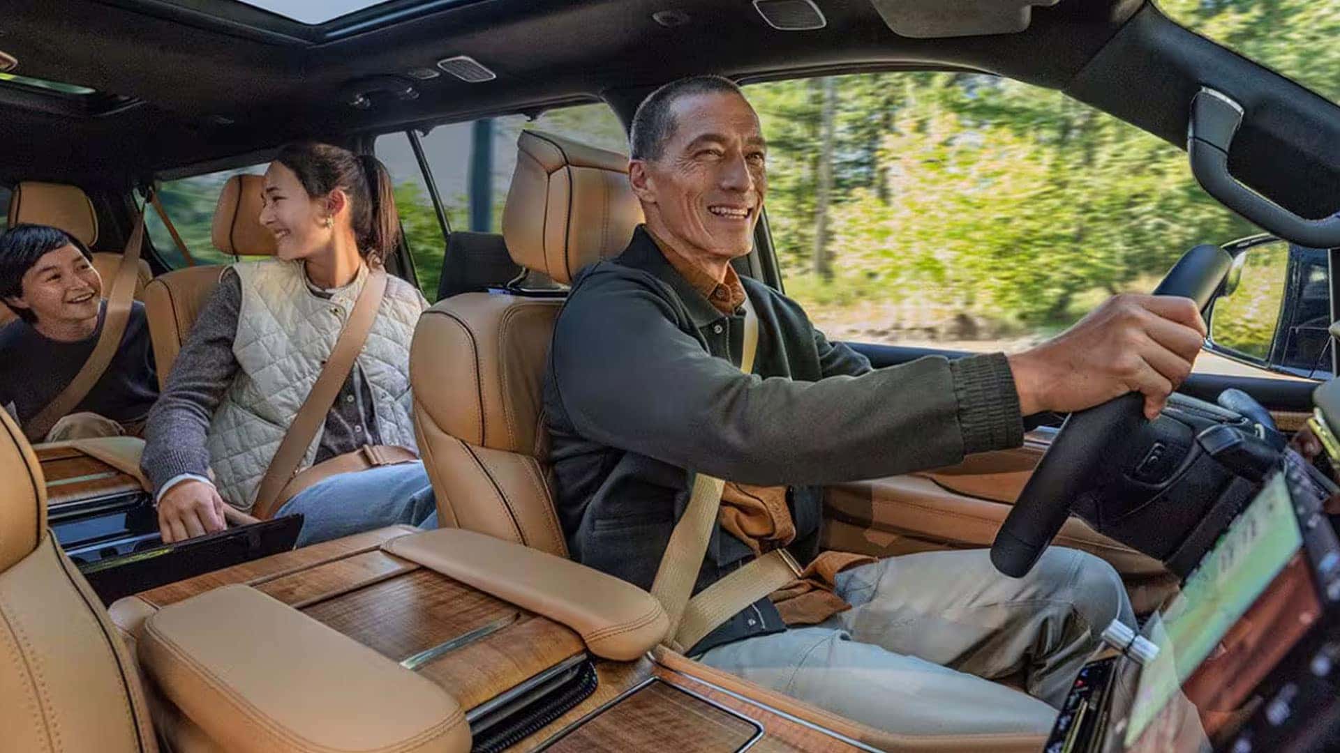 2026 Jeep Grand Wagoneer cabin with tan leather seats, wood trim, panoramic roof, driver, and two passengers.