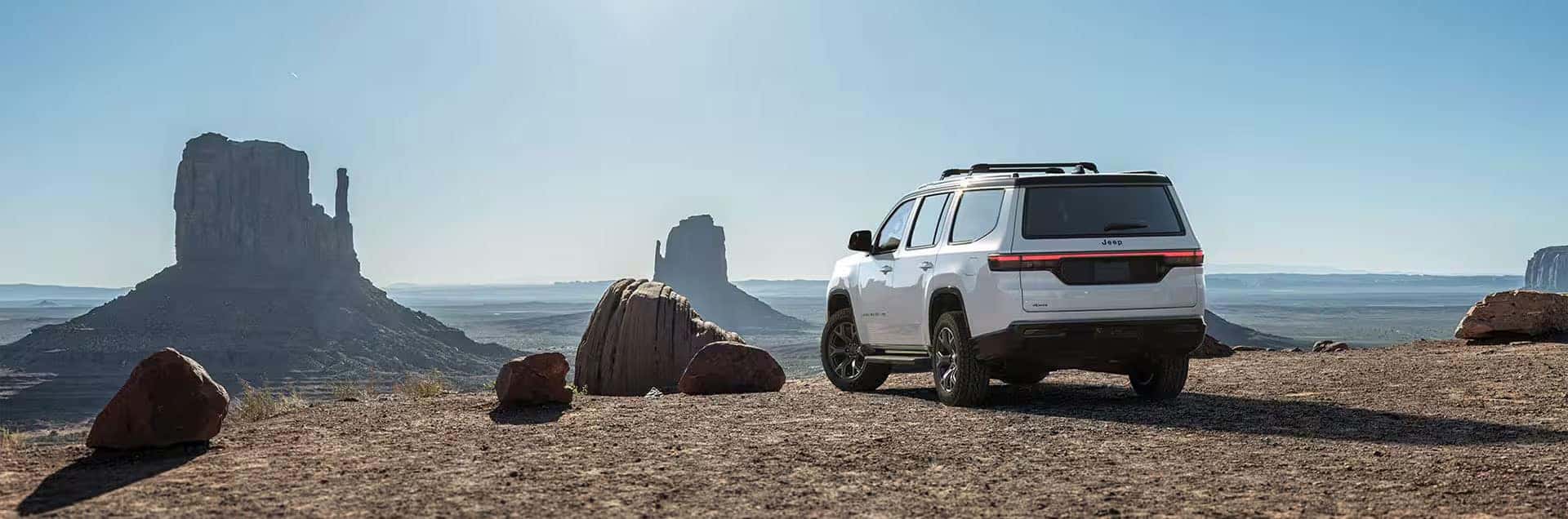 2026 Jeep Grand Wagoneer parked on a rocky desert overlook with tall sandstone formations in the distance.