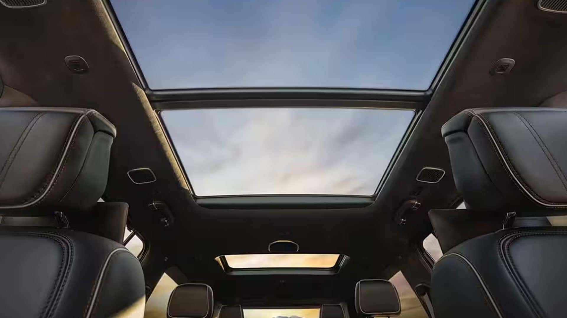 Interior view of a 2026 Jeep Grand Wagoneer showing the large panoramic glass roof above black leather seats.