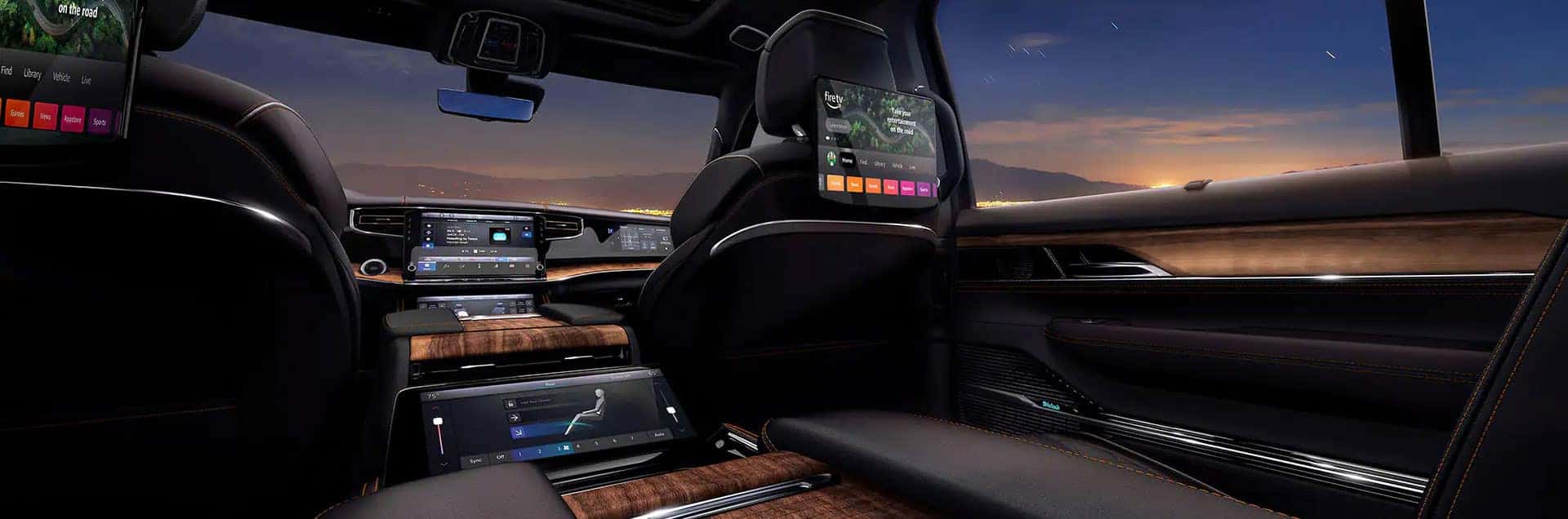 Wide interior view of a 2026 Jeep Grand Wagoneer with black leather seats, wood trim, and rear entertainment screens.