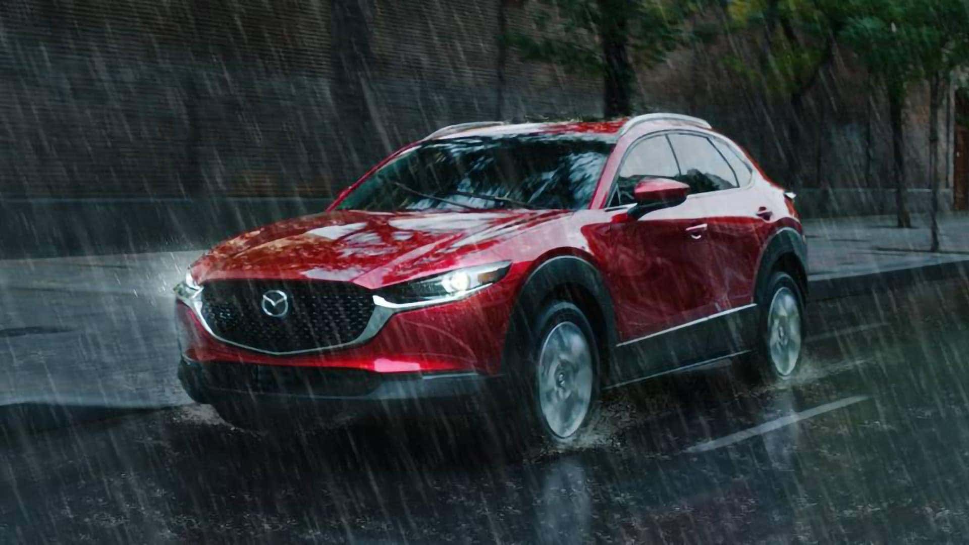 Red 2026 Mazda CX-30 driving through heavy rain with its LED headlights illuminated