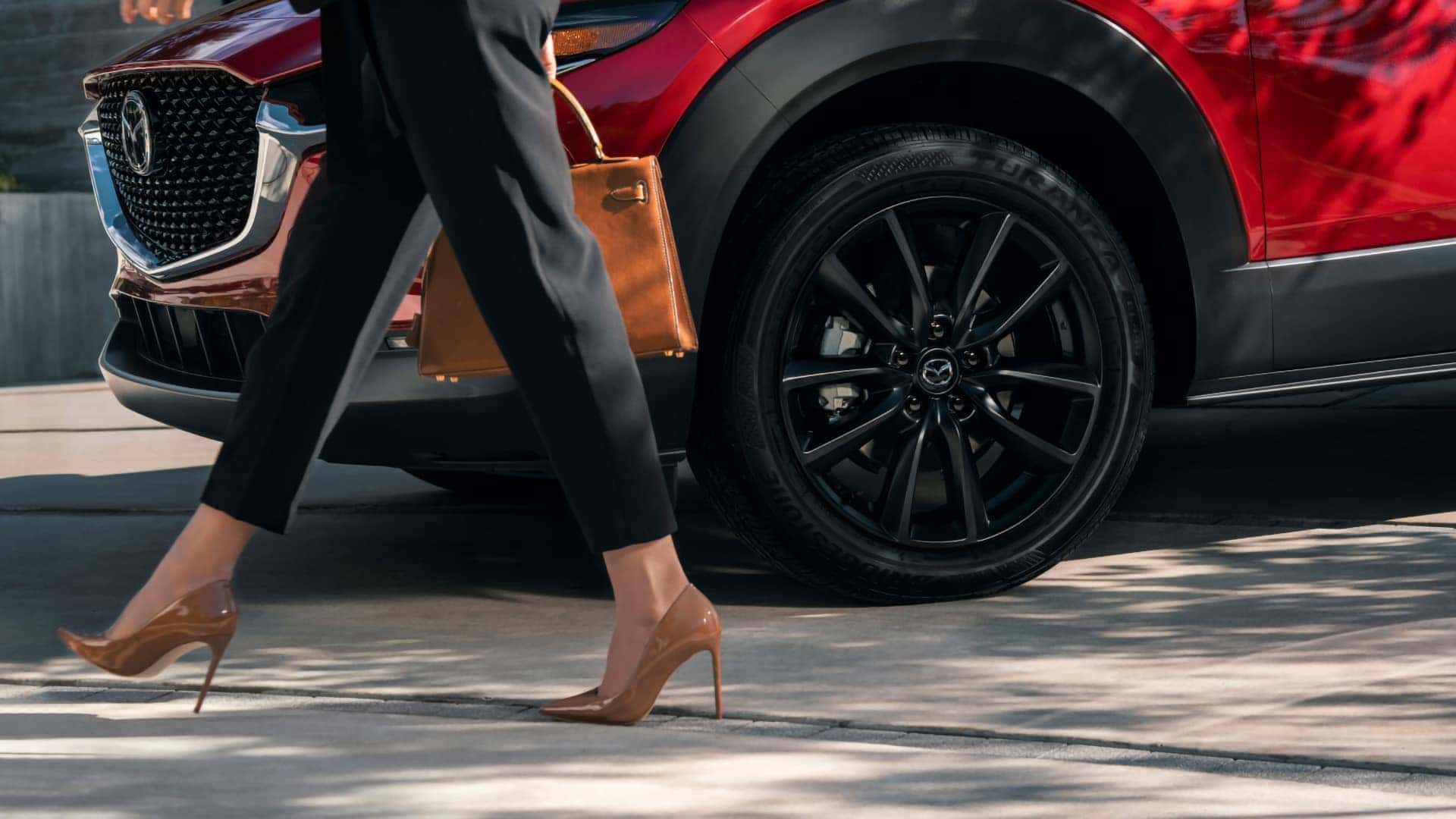 Close-up of a black alloy wheel on a red 2026 Mazda CX-30 parked along a sidewalk