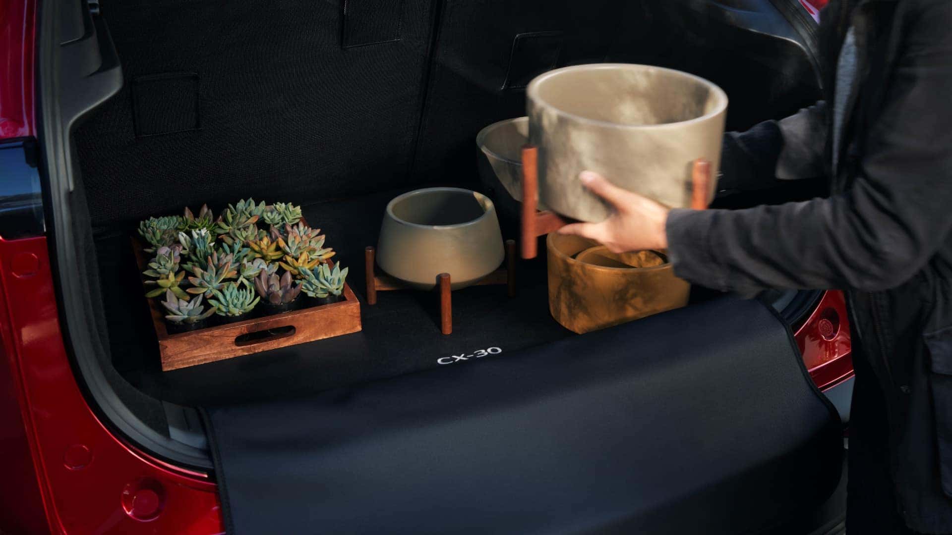 Person loading planters and succulents into the cargo area of a red 2026 Mazda CX-30
