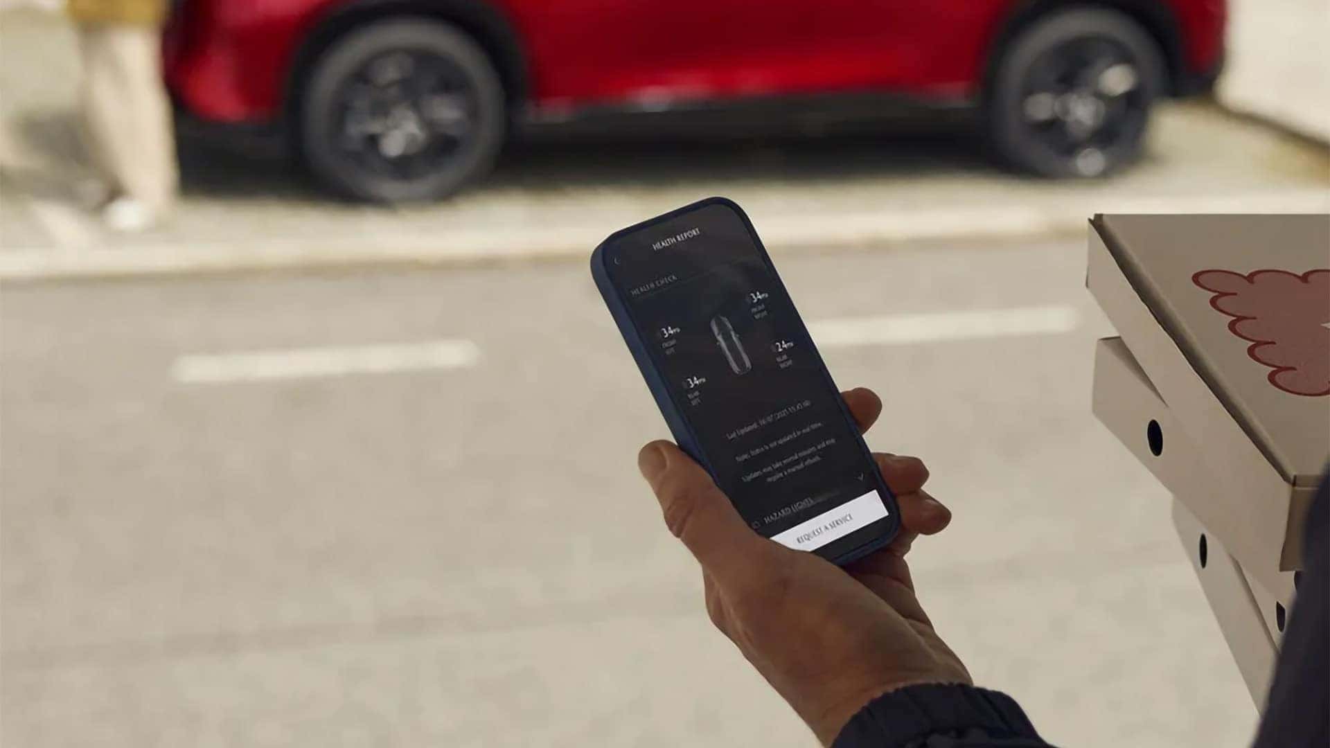 Driver checking vehicle status in the MyMazda App with a red 2026 Mazda CX-5 nearby