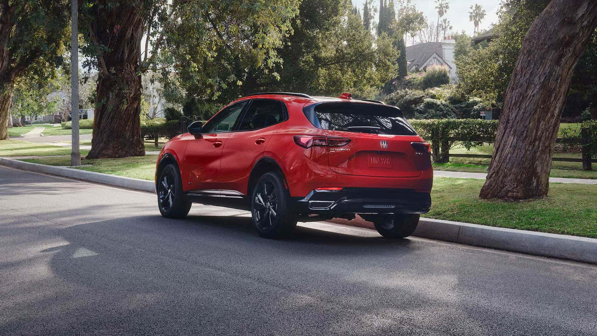 Red 2026 Buick Envision Sport Touring in rear three-quarter view on a tree-lined street