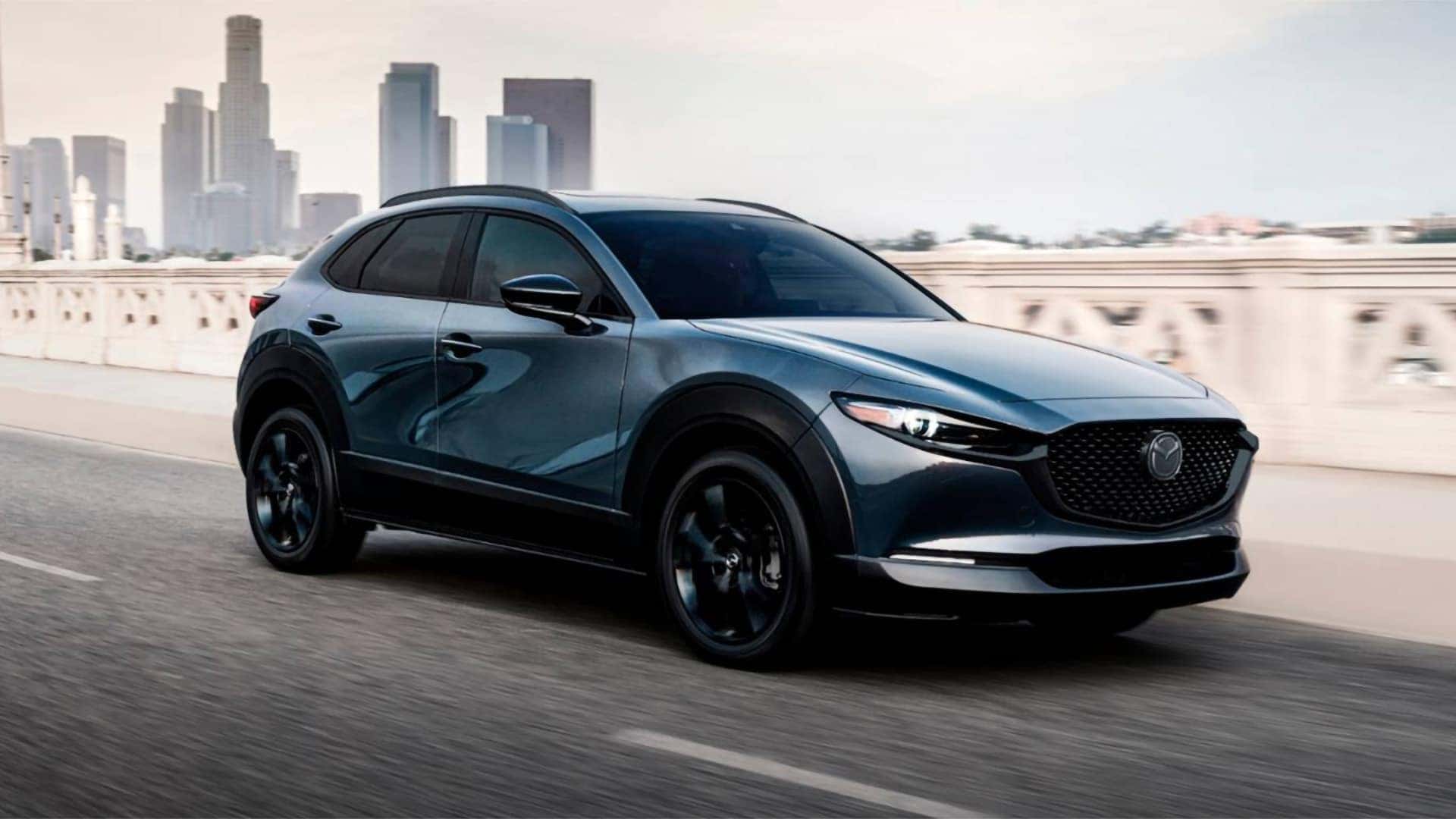 Blue 2026 Mazda CX-30 driving across a city bridge, shown from the front three-quarter angle