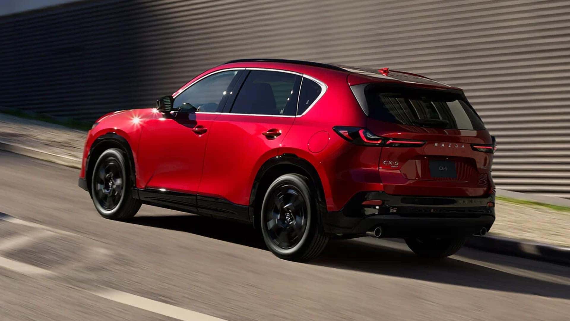 Red 2026 Mazda CX-5 driving on a paved road, shown from the rear three-quarter angle