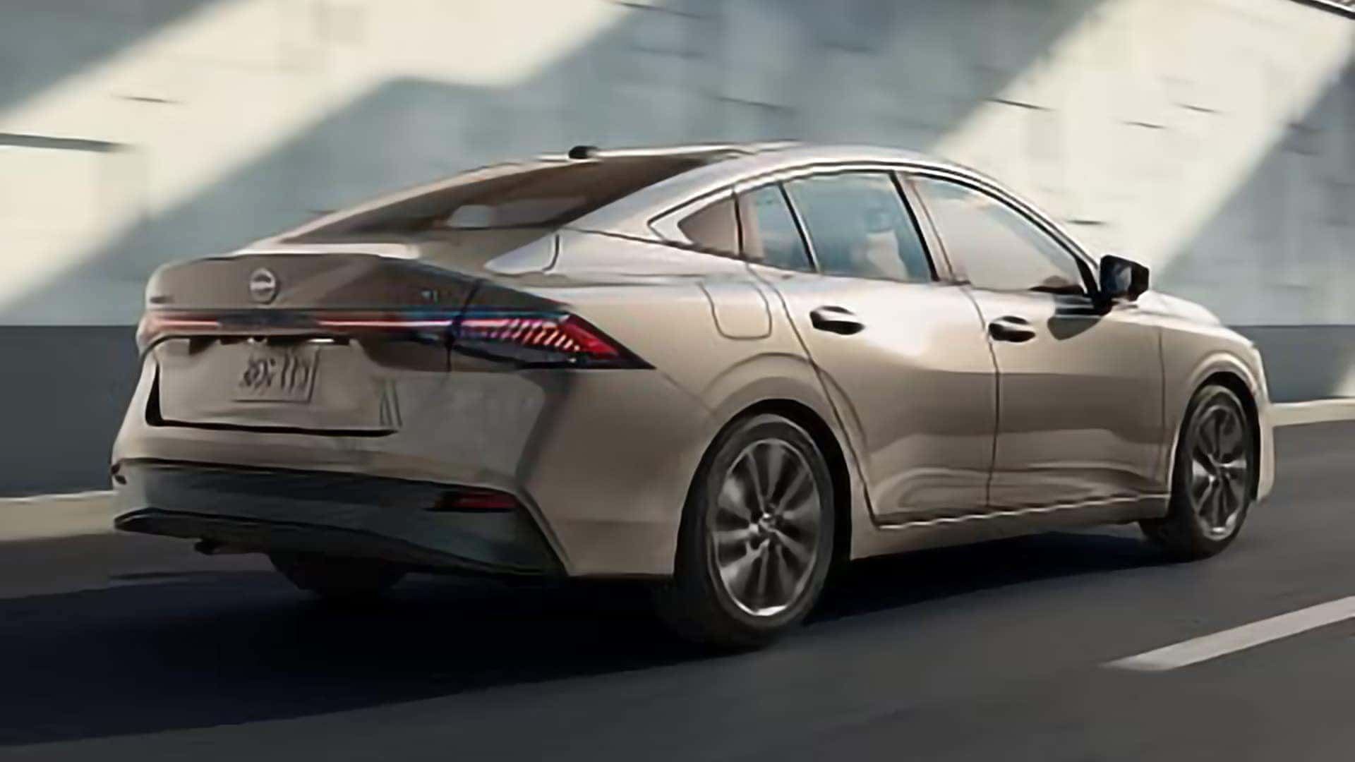 2026 Nissan Sentra driving on a city road, shown from the rear three-quarter angle.