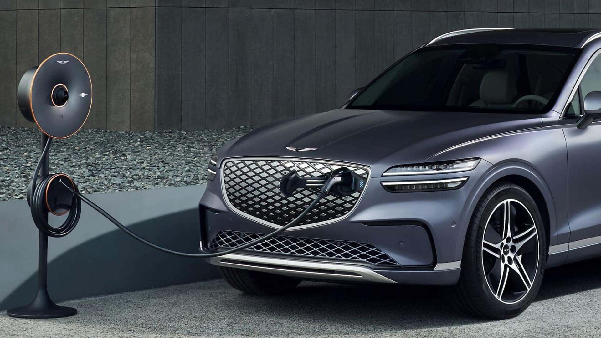 2026 Genesis Electrified GV70 connected to a home charging station through its front grille charging port