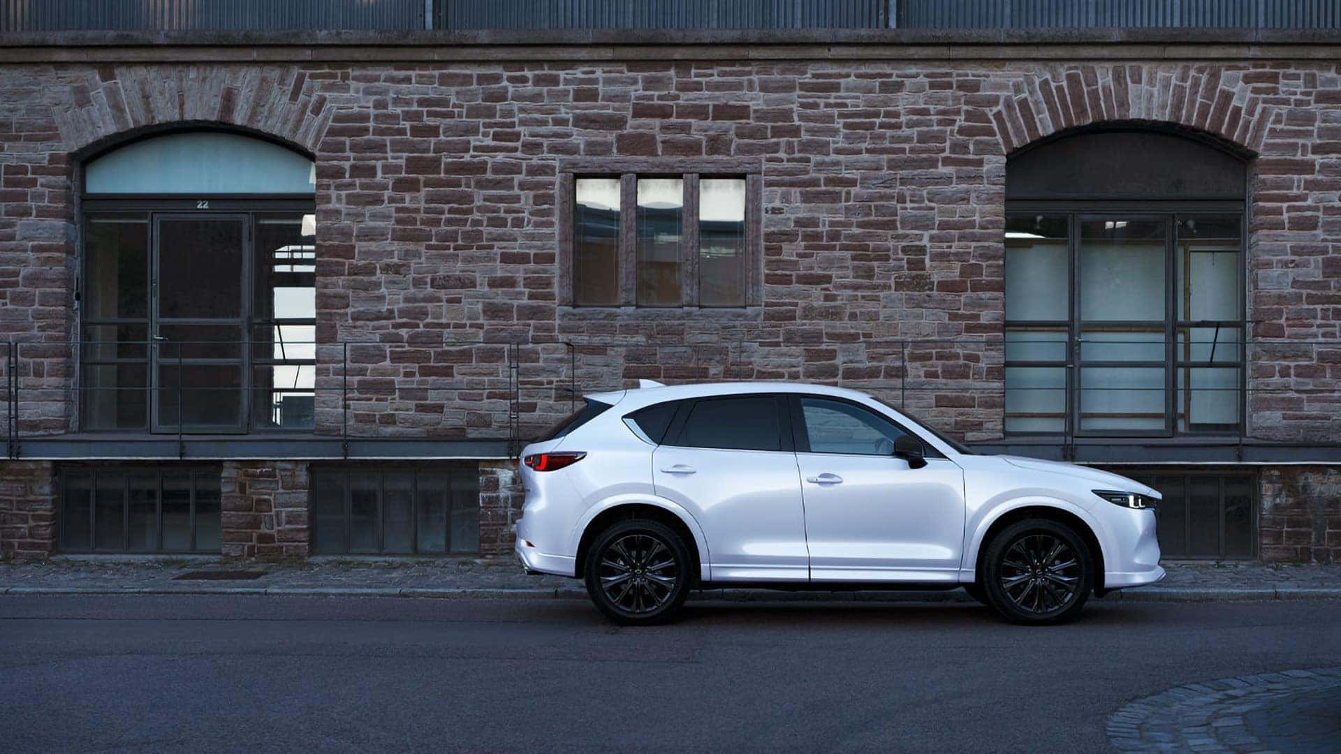 White 2026 Mazda CX-5 in side profile parked beside a stone building