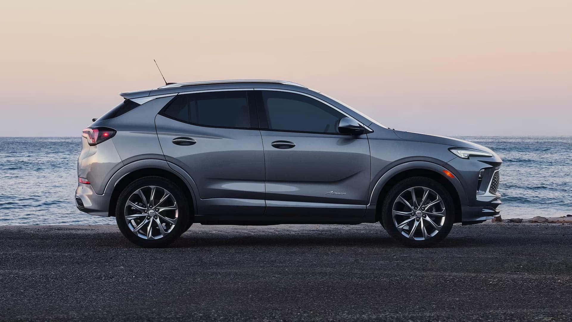 Side profile of a gray 2026 Buick Encore GX Avenir parked beside the ocean