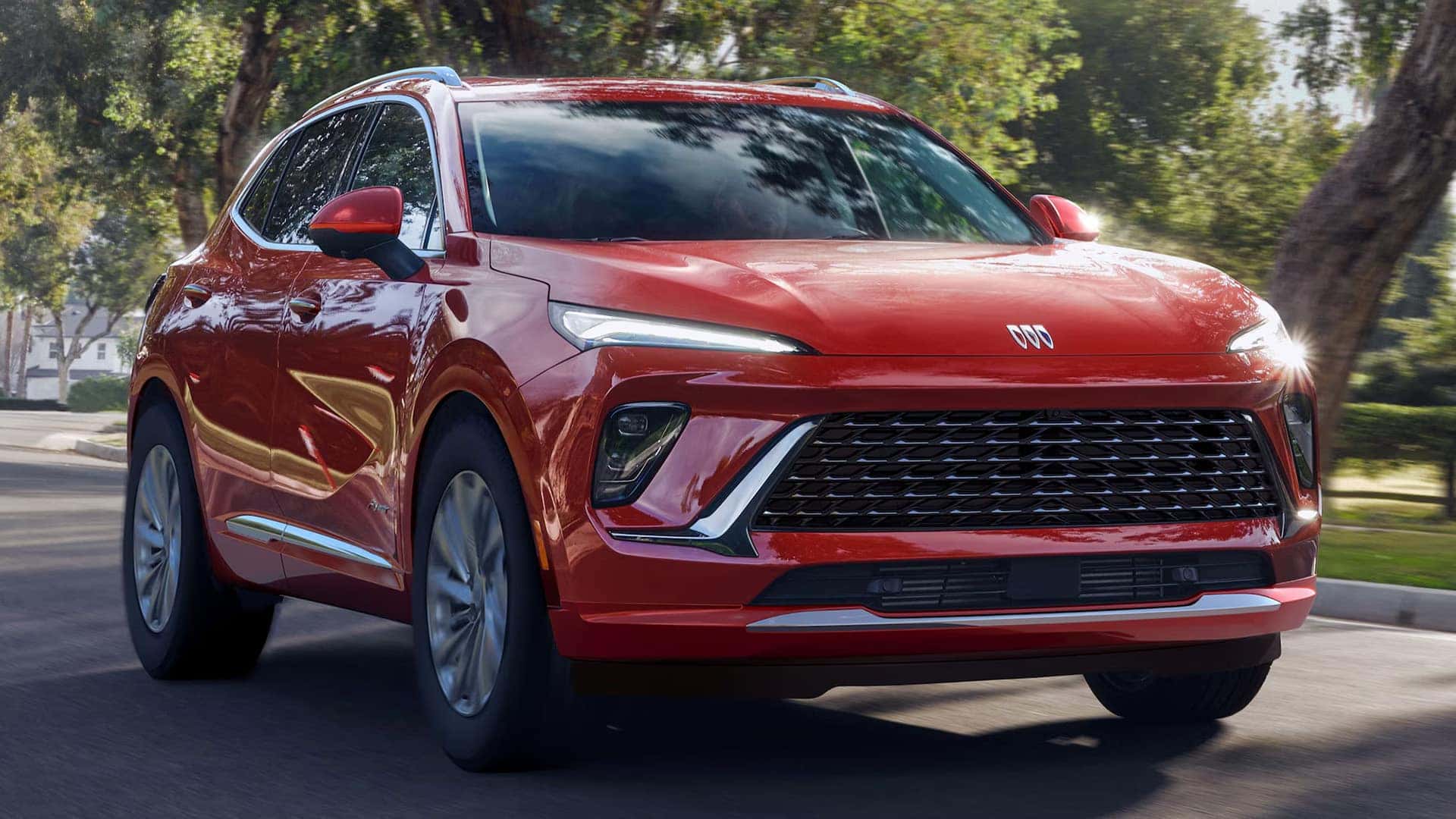 Front three-quarter view of a red 2026 Buick Envision driving on a tree-lined road