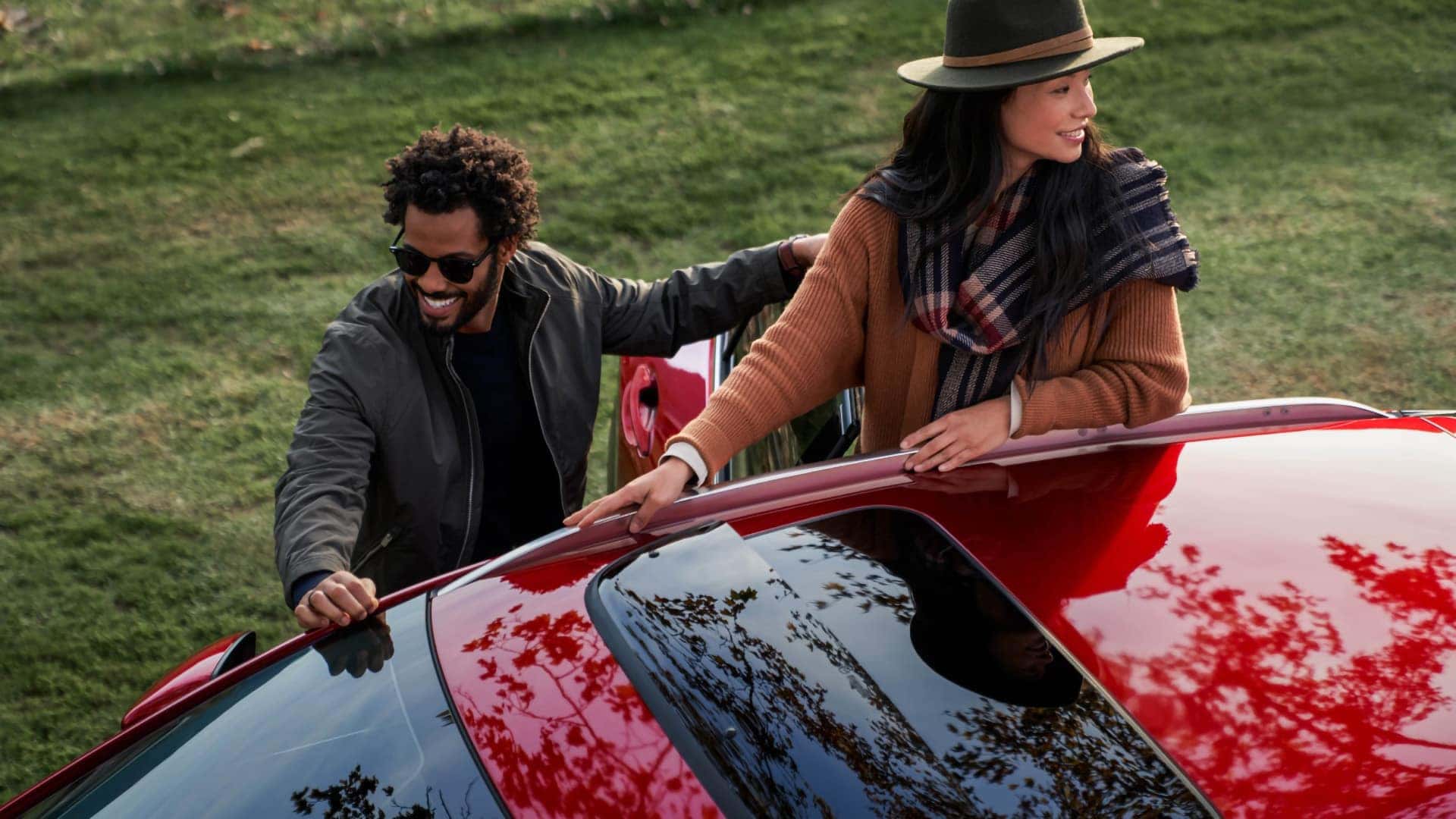 Two people standing beside a red 2026 Mazda CX-30 and examining its silver roof rails