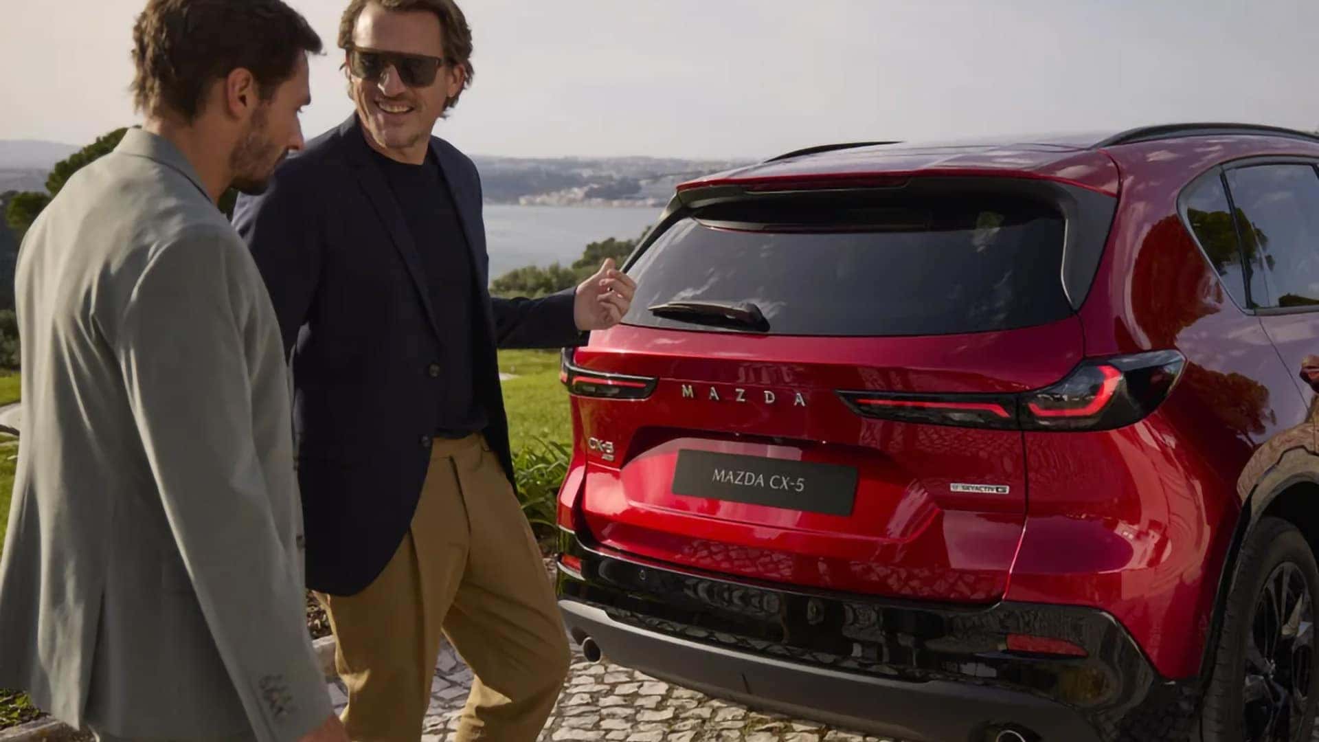 Two people standing beside the rear of a red 2026 Mazda CX-5