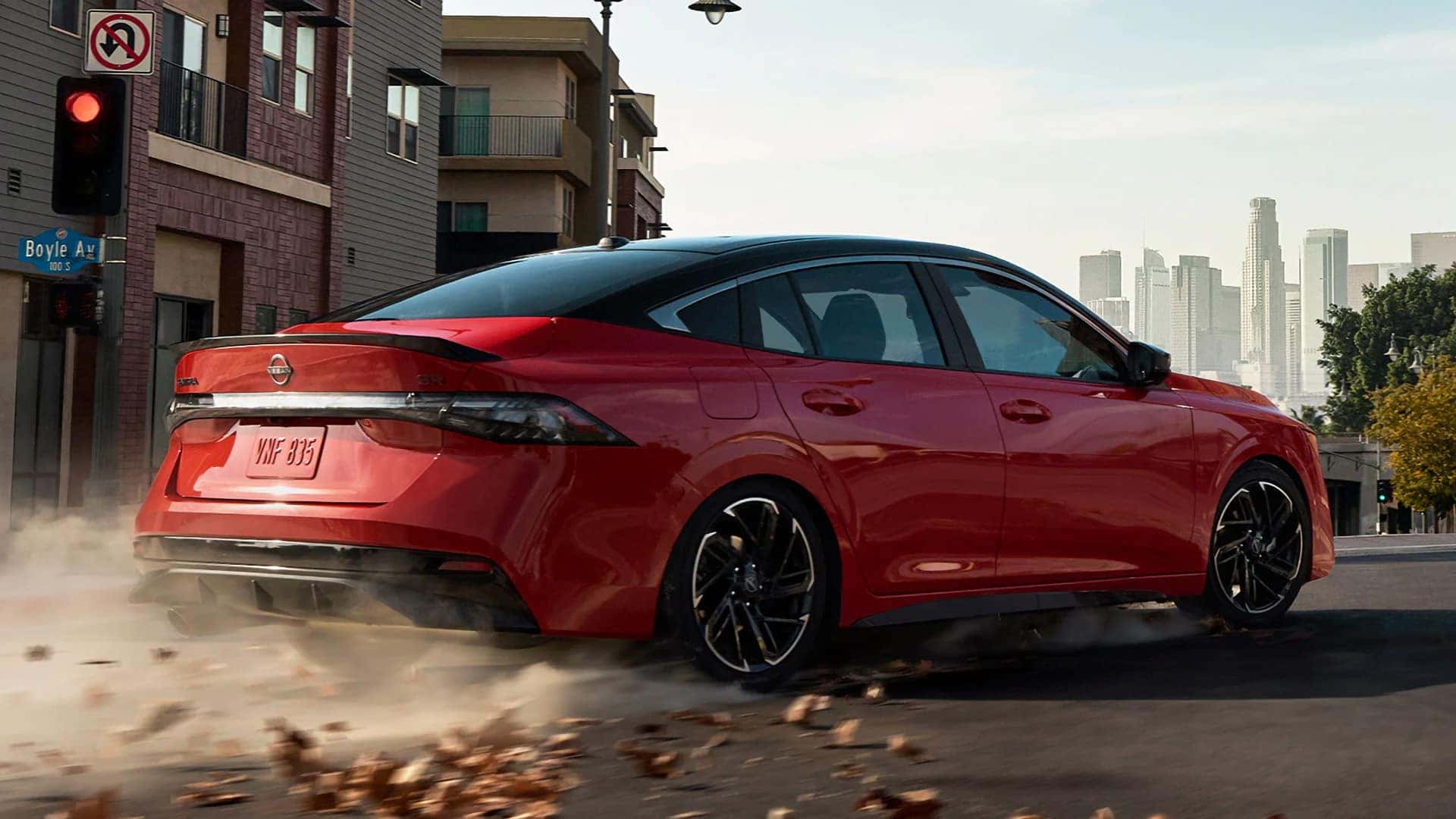Red 2026 Nissan Sentra SR driving through a city in a rear three-quarter exterior view