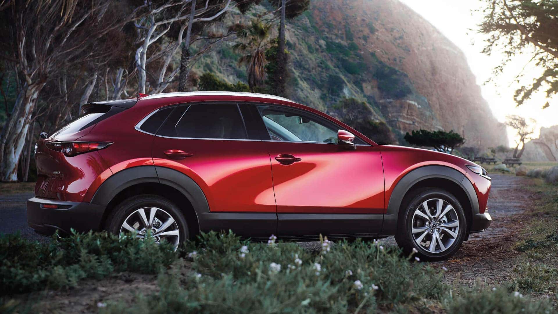 Red 2026 Mazda CX-30 shown in profile beside trees and a rocky mountain landscape
