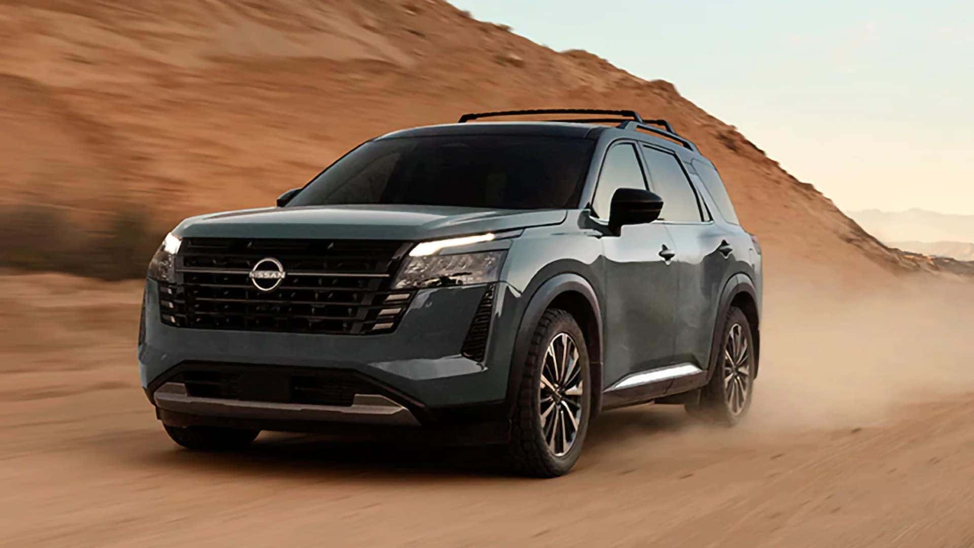 Green 2026 Nissan Pathfinder driving on a dusty desert road with roof rails and black exterior accents