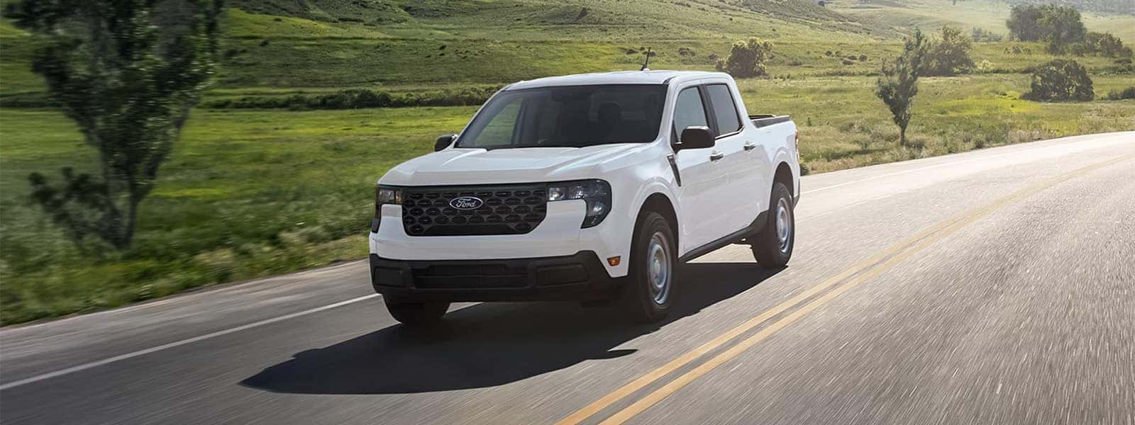 White 2026 Ford Maverick pickup driving on a road through green hills
