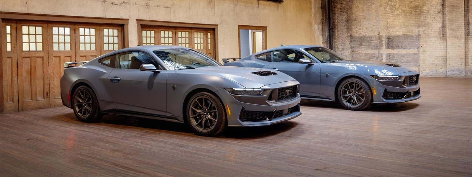 Two 2026 Ford Mustang models displayed inside an industrial-style showroom