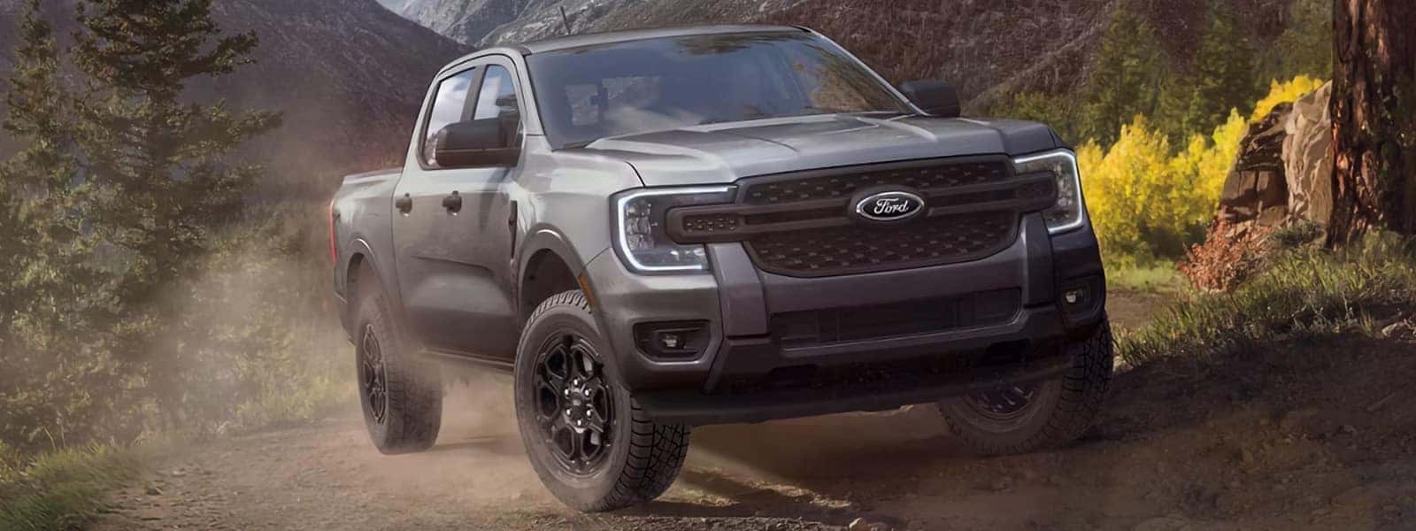 Gray 2026 Ford Ranger driving on a mountain trail with rugged terrain in the background