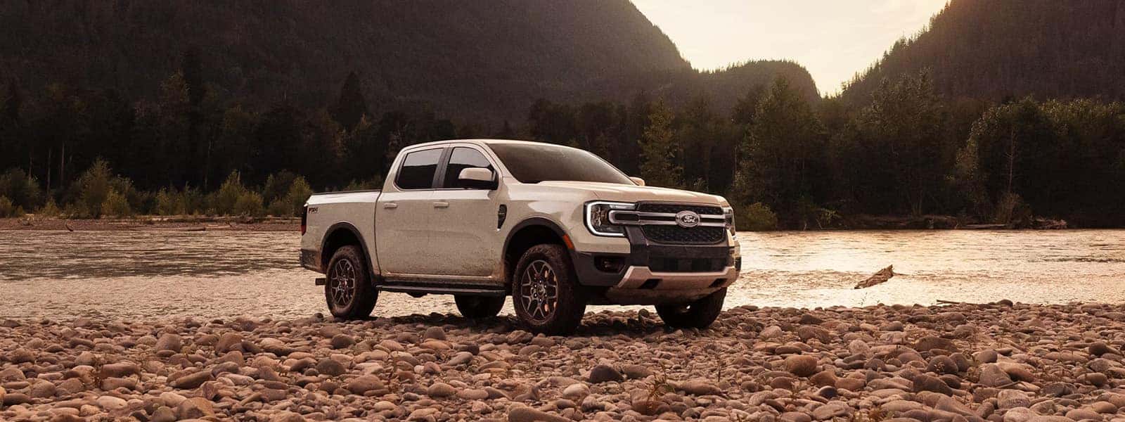 White 2026 Ford Ranger parked on a rocky riverbank with mountains in the background
