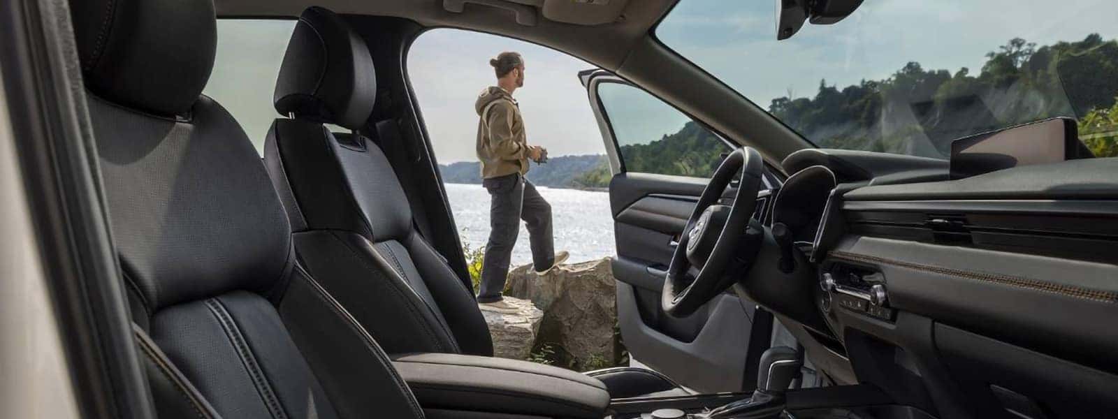 Black front seats and dashboard inside the 2026 Mazda CX-50 Hybrid overlooking a lakeside landscape