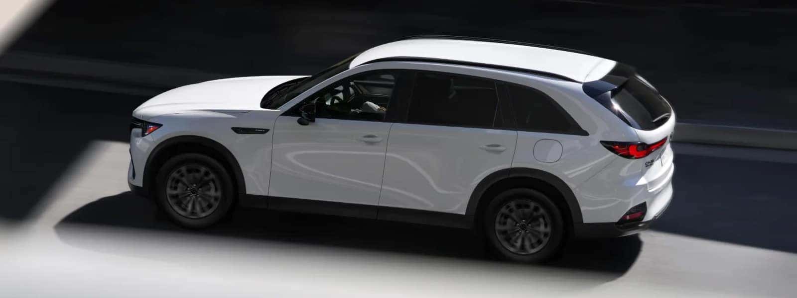 White 2026 Mazda CX-70 PHEV driving through a shaded roadway in side profile