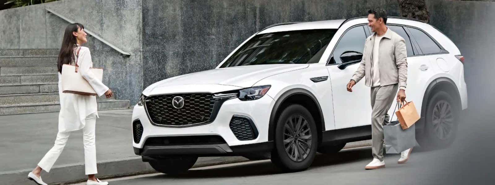 White 2026 Mazda CX-70 PHEV parked at the curb as two people approach with shopping bags
