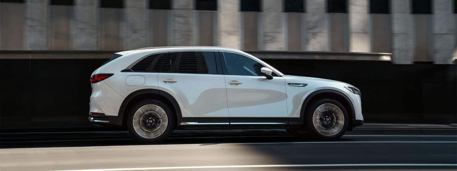 White 2026 Mazda CX-90 PHEV driving through the city in side profile