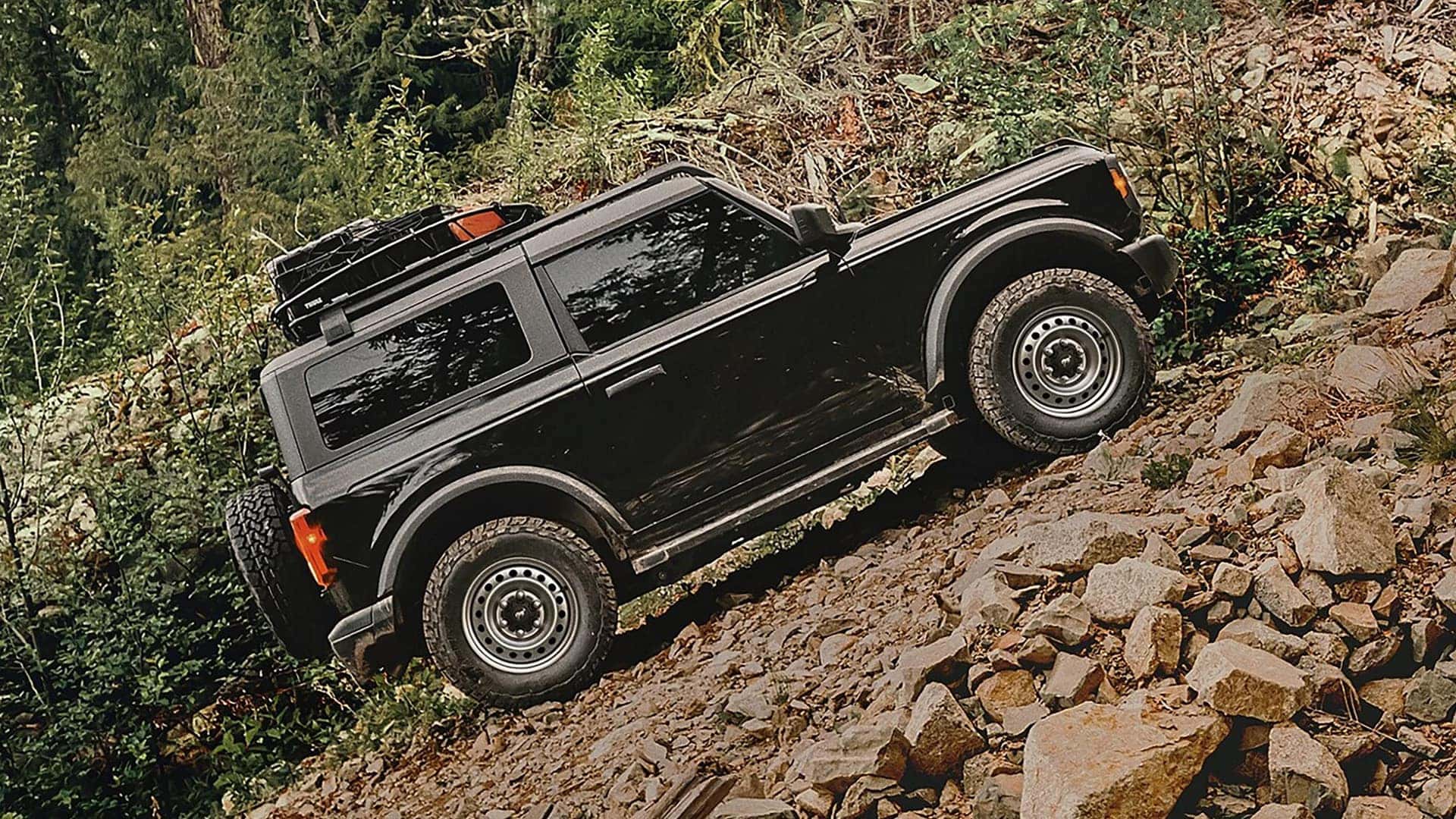 Black two-door 2026 Ford Bronco climbing a steep rocky trail with a roof-mounted cargo basket