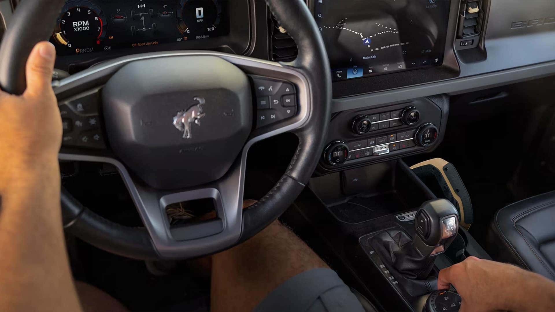 Driver operating the steering wheel and four-wheel-drive controls inside a 2026 Ford Bronco