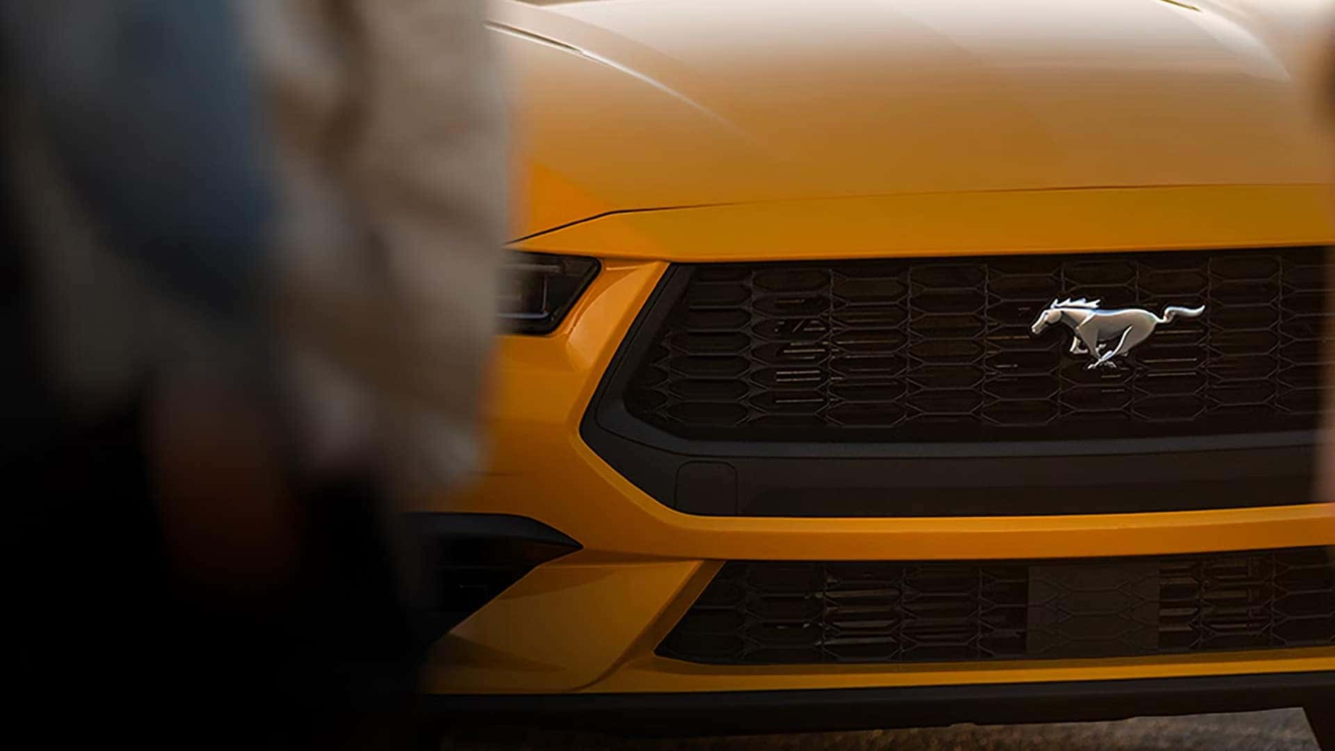 Close-up of the black grille and Mustang pony emblem on an orange 2026 Ford Mustang