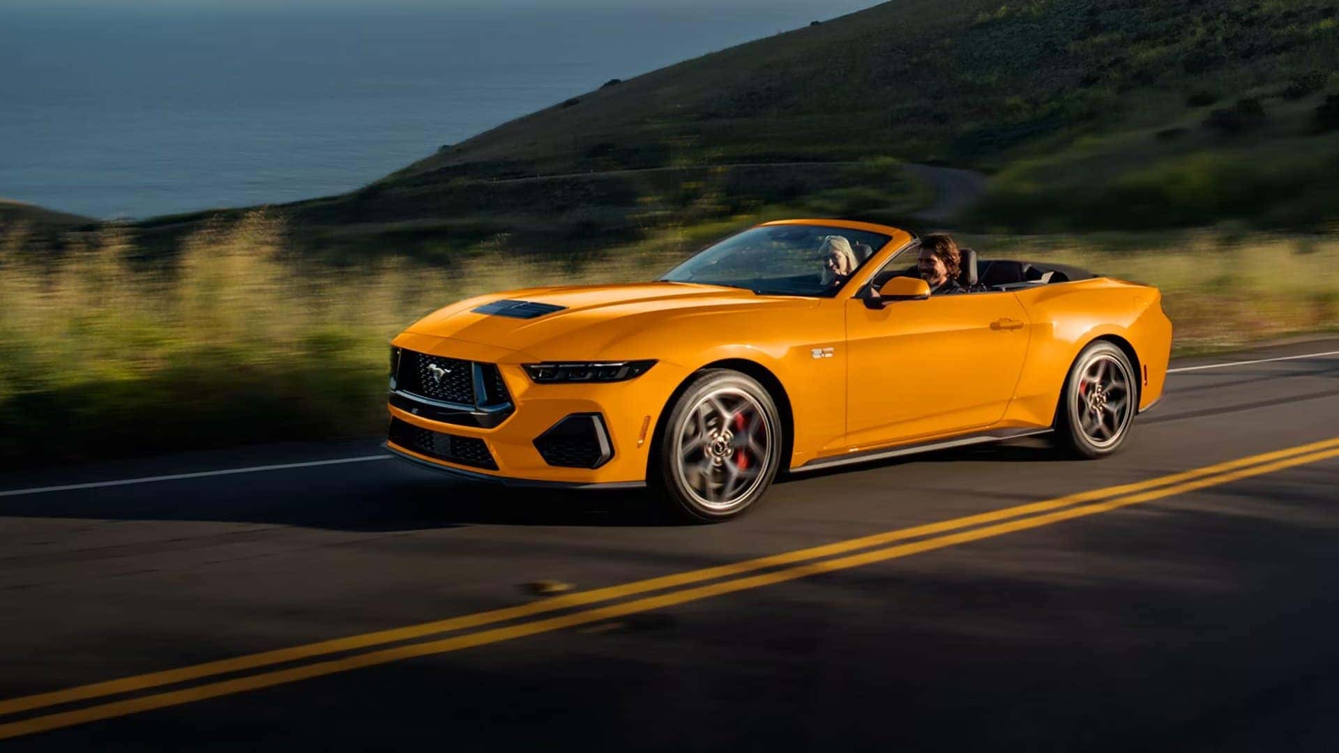 Orange 2026 Ford Mustang GT Convertible driving on a coastal road