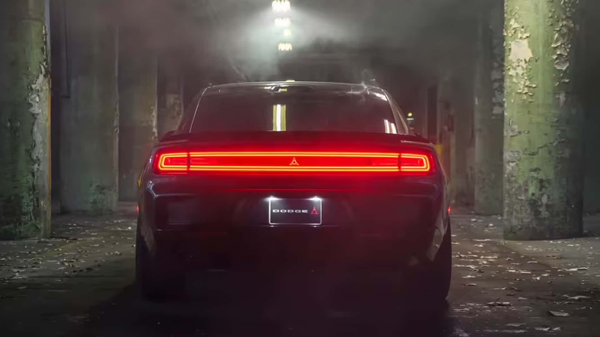 Rear view of a dark Dodge Charger with a full-width red light bar inside a worn industrial building.
