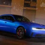 Blue four-door Dodge Charger at a front three-quarter angle with bright white front lighting illuminated.