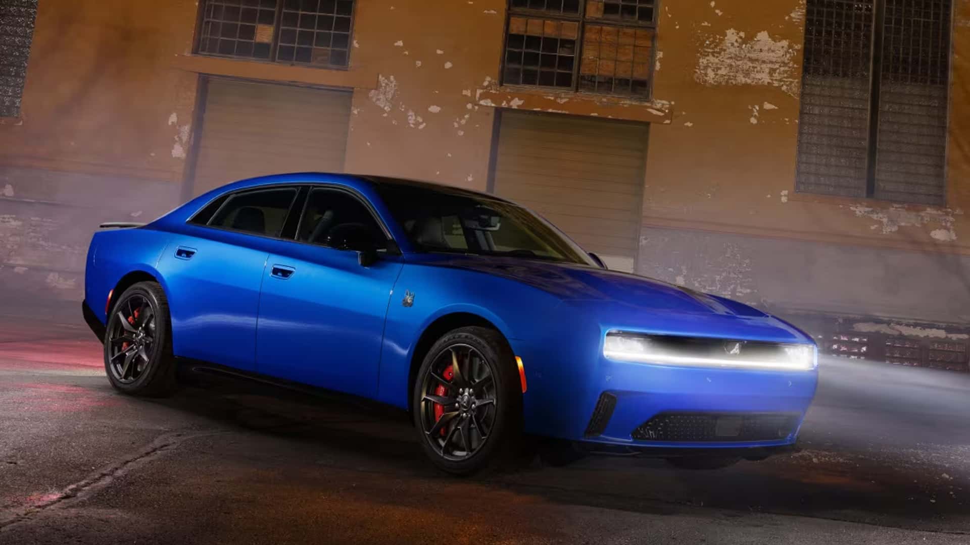 Blue four-door Dodge Charger at a front three-quarter angle with bright white front lighting illuminated.
