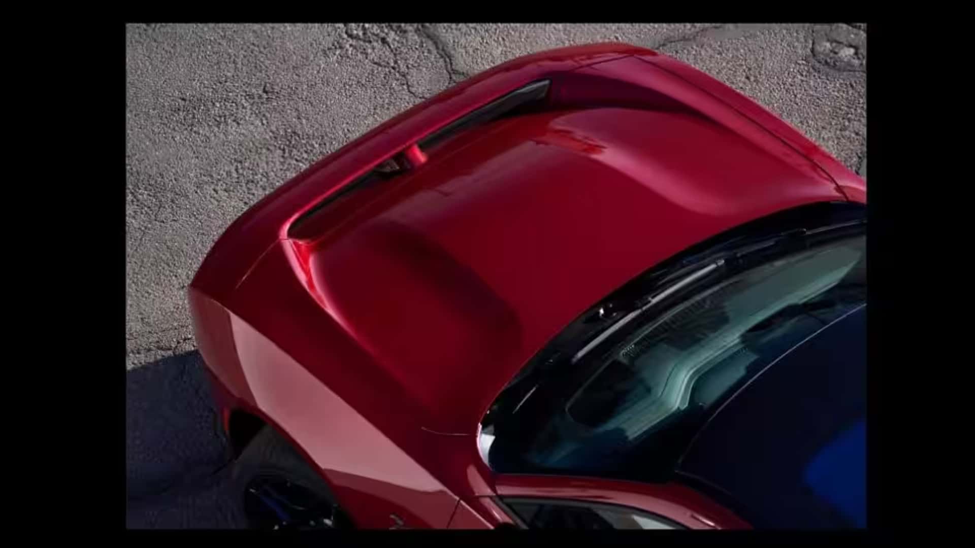 Overhead close-up of a red Dodge Charger hood with a raised center section and narrow opening near the front.