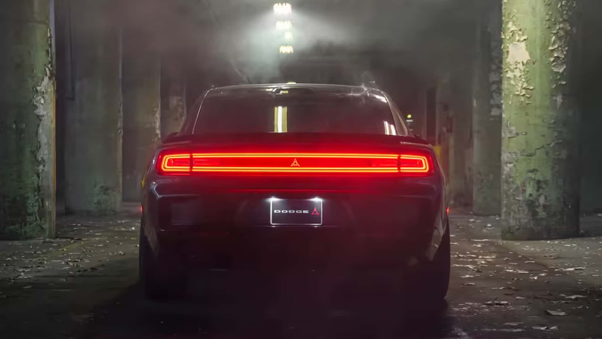 Rear view of a dark Dodge Charger with a glowing full-width red light bar inside an industrial building.
