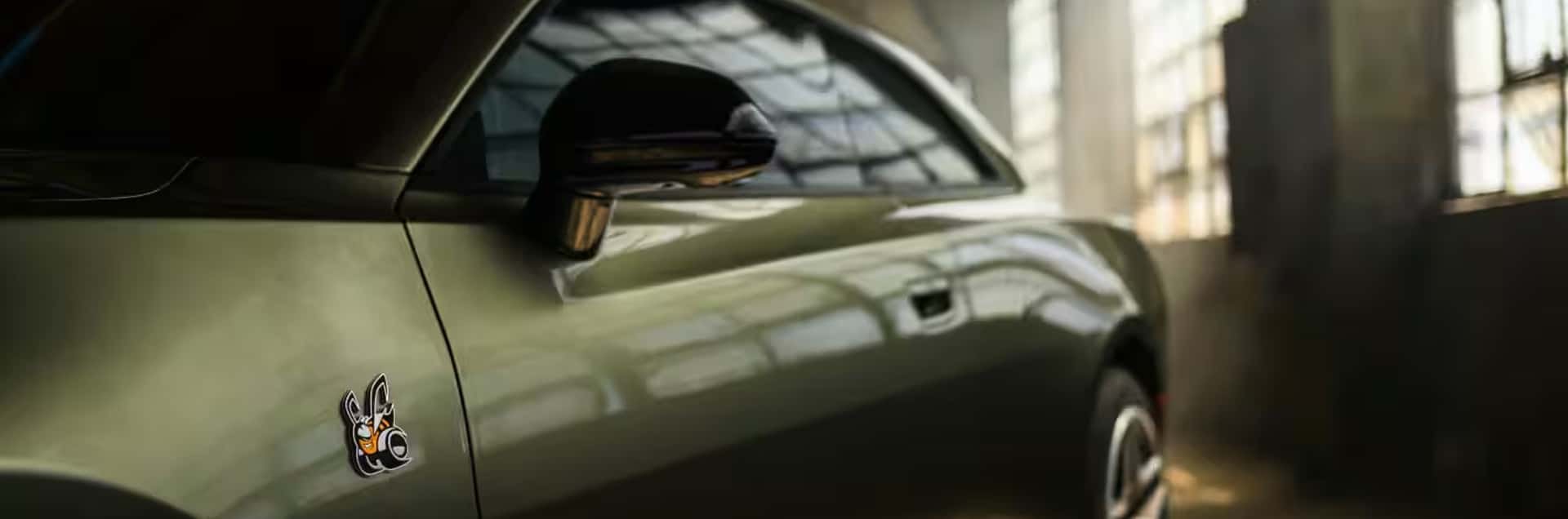 Close-up of a green Dodge Charger side panel with bee badge, black mirror, tinted window, and flush door handle.